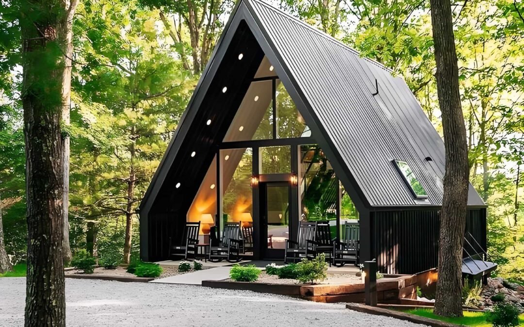 A Frame Cabin With Large Windows, Surrounded By Trees. A Gravel Path Leads To The Entrance, And There's Outdoor Seating On The Porch.
